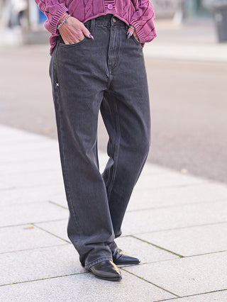 FDL Jeans Brooklyn Black: Person trägt weite, gewaschene schwarze Jeans auf dem Bürgersteig, Hände in den Taschen, kombiniert mit schwarzen Lederschuhen und einem Strickpullover.