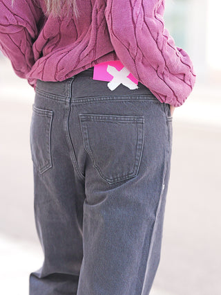 FDL Jeans Brooklyn Black: Das Bild zeigt die Rückseite einer Person in locker sitzender, grauer Wide Leg Denim mit auffälligem pinkfarbenem Patch am Bund, kombiniert mit einem dicken Strickpullover.