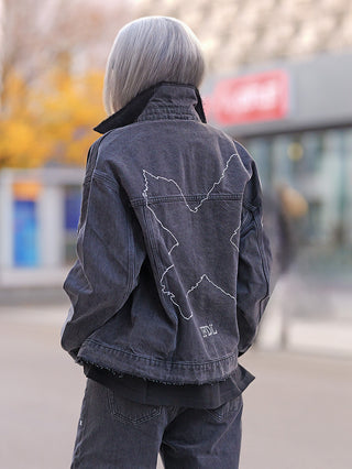 Person trägt FDL Denim Jacket Chicago black: weite, schwarze Jeansjacke mit großem, weißen „X“-Stitching und „FDL“-Stickerei hinten. Kombiniert mit passenden Jeans, urbaner Stil.