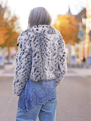 Die OFF#DLY Fake Fur Jacke black/white zeigt eine Person von hinten, die die kurz geschnittene, luxuriös weiche Kunstfelljacke mit Animal-Muster trägt, stilvoll kombiniert mit blauer Spitze und Jeans.