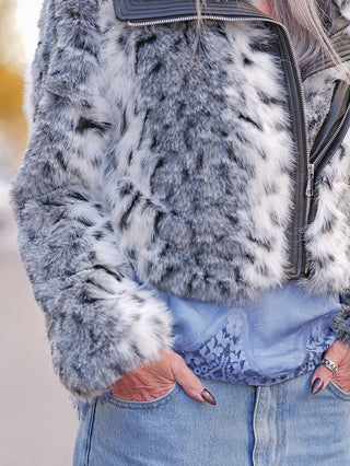 Nahaufnahme der OFF#DLY Fake Fur Jacke black/white mit luxuriösem Kunstfell und kurzem Schnitt, getragen über einem Spitzen-Top, kombiniert mit mittelblauen Jeans, Hände in den Taschen mit dunklem Nagellack.