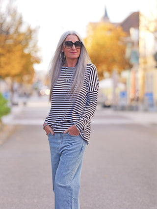 Eine Frau trägt das OFF#DLY Ringelshirt mit Rundhals und geschnittenen Kanten in braun/weiß. Das locker sitzende Langarmshirt ergänzt ihren lässigen Look mit Jeans und Accessoires.