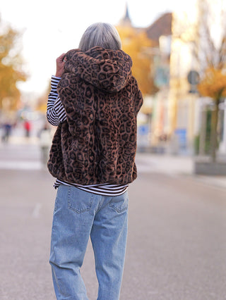 Person von hinten mit der Off#DLY Fake Fur Weste Leo brown, einem lässigen Leopardenmuster-Gilet mit Kapuze, über einem gestreiften Shirt und Jeans, ideal für herbstliche Tage.