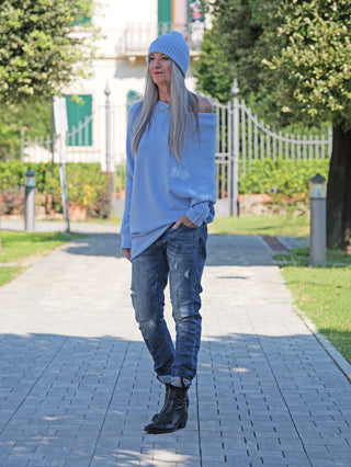 Person trägt OFF#DLY Denim Ines Midblue Destroy Jeans mit leichten Destroy-Details und authentischer Waschung, kombiniert mit schwarzen Stiefeletten und einem hellblauen, schulterfreien Pullover.