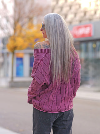 Person mit langen, grauen Haaren trägt eine OFF#DLY West Ada bordeaux im Oversize-Look mit auffälligem Strickmuster, kombiniert mit dunklen Jeans auf einem Bürgersteig.