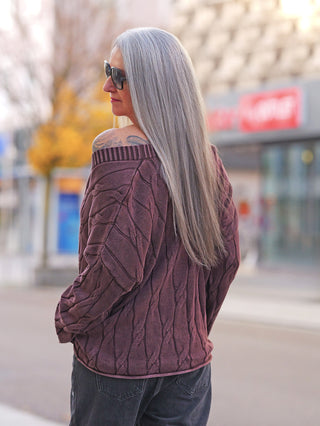 Ältere Frau trägt stilvoll OFF#DLY West Ada braun Strickweste mit markantem Strickmuster und V-Ausschnitt, zeigt modernen, lässigen Stil. Tattoo und Herbstumgebung ergänzen den Look.