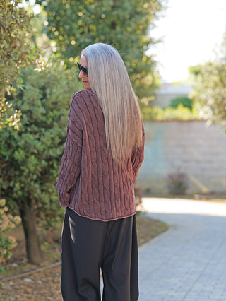 Frau trägt den OFF#DLY Pulli Aida schoko, einen lässigen, oversized, braunen Strickpullover mit strukturierter Musterung, kombiniert mit weiten schwarzen Hosen, ideal für einen modernen, entspannten Look.