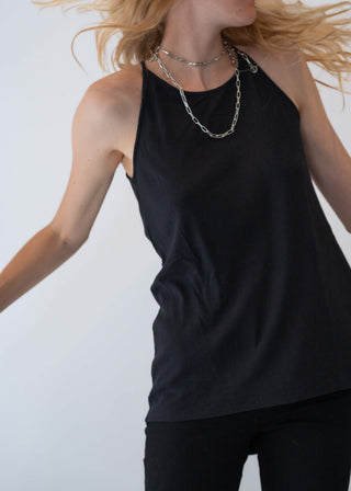 Person trägt ein schwarzes Outryght Tina Top ohne Ärmel, kombiniert mit einer mehrlagigen Silberkette. Das Top besteht aus einem RIB-Materialmix aus Baumwolle, Modal und Elasthan.