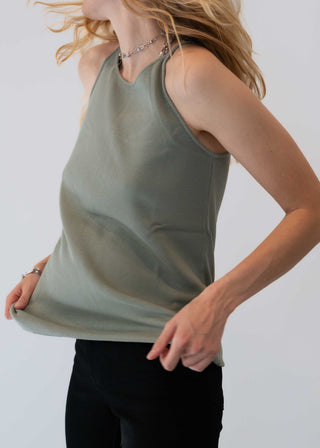 Person trägt das Outryght Tina military green Tanktop in geripptem Design, kombiniert mit schlanken schwarzen Hosen. Das ärmellose Top hat einen Rundhalsausschnitt. Sichtbare Accessoires sind eine silberne Halskette und Armband.