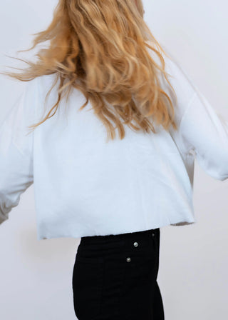 Person mit langen, welligen blonden Haaren trägt das Outryght Kushi white dove, ein kastiges, weißes Langarmoberteil mit leicht rohem Saum, kombiniert mit hoch taillierten schwarzen Jeans, von hinten gesehen.