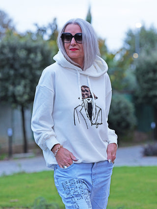 Person trägt den OFF#DLY Sweat Women white, einen lockeren Off-White-Hoodie mit minimalistischem Print einer Figur im Hut, kombiniert mit hellen Jeans und schwarzen Textdetails.