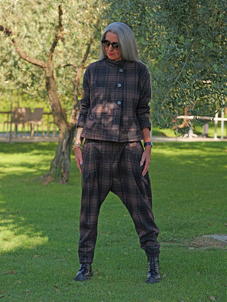 Ältere Frau, die im Freien OFF#DLY Pant Lilly kariert braun/grau trägt; locker geschnitten, modernes Karomuster, kombiniert mit schwarzen Schnürstiefeln und Accessoires für stilvollen, entspannten Look.