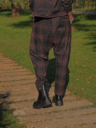 OFF#DLY Pant Lilly kariert braun/grau zeigt eine lässige, moderne Hose mit leicht ballonförmigem Schnitt und elastischem Bund, getragen von einer Person zu Boots auf einem Steinweg.