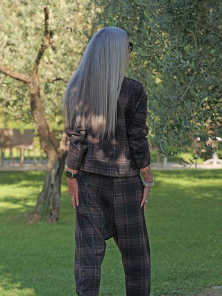 Person im Freien trägt die OFF#DLY Jacke Layla kariert braun/grau, mit modernem, boxy Schnitt und Stehkragen, kombiniert mit passender Hose. Sichtbar: Smartwatch, Ringe, Armbänder, kleines Tattoo.