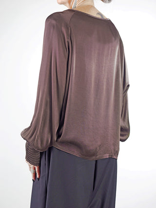 Das Modell trägt das OFF#DLY LS Shirt Valentina braun mit weiten, smockierten Ärmeln. Der fließende Viskosestoff verleiht dem Shirt Eleganz, ideal für stilvolle oder lässige Anlässe.