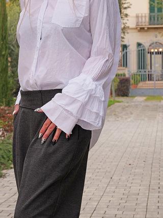 Person trägt die OFF#DLY Bluse Viola white mit verspielten Volant-Ärmeln, kombiniert mit dunklen Hosen. Hände auf Hüften, Nägel in Schwarz und Tiermuster-Design.