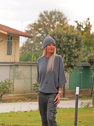 Frau trägt den OFF#DLY Pulli Ellen Asphalt mit lockerer Passform und Fledermausärmeln, kombiniert mit schwarzen Cargo-Hosen und einer grauen Mütze, für einen lässig-eleganten Look.