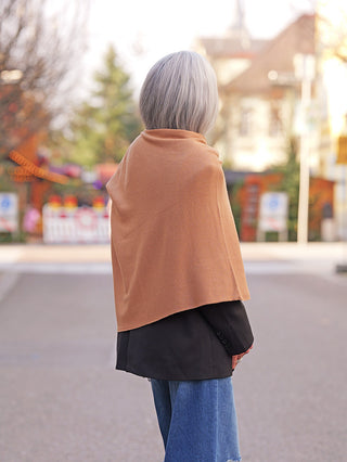 Person trägt den OFF#DLY Poncho Lilly camel über einem schwarzen Blazer. Der Poncho fällt asymmetrisch und verleiht dem Outfit einen eleganten, fließenden Look, ideal für Übergangszeiten.