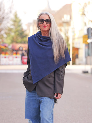 Eine modisch gekleidete Frau trägt den OFF#DLY Poncho Lilly marine über einem Blazer, kombiniert mit hellblauen Jeans, zeigt den eleganten, fließenden Fall des weichen, asymmetrischen Ponchos.