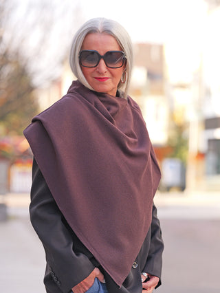 Ältere Frau trägt den OFF#DLY Poncho Lilly schoko über einem dunklen Blazer, der elegant drapiert und fließend fällt, während sie auf einer Stadtstraße steht.