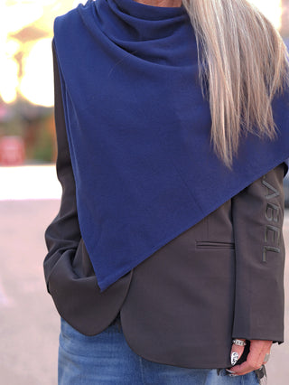 Person trägt den OFF#DLY Poncho Lilly marine über einem dunklen Blazer, mit einer Hand in der Jeanstasche. Sichtbar sind weiße Nägel mit schwarzem Design und silberne Ringe.