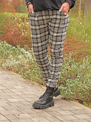 OFF#DLY Joggpant The Checker black in modernem Karo-Design, getragen von einer Person auf einem Gartenweg, kombiniert mit schwarzen, klobigen Schnürstiefeln für einen stilvollen, bequemen Alltagslook.