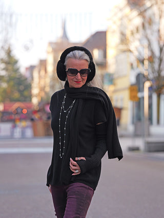 Eine Frau trägt die OFF#DLY Ohrwärmer black aus weichem Fake Fur, während sie durch eine urbane Straße spaziert. Die Ohrwärmer passen perfekt zu ihrem stilvollen, schwarzen Outfit.