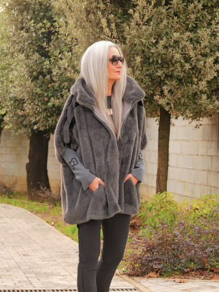 Person mit langen, silbernen Haaren trägt die OFF#DLY FakeFur Jacke Rom asphalt, eine voluminöse Kunstpelzjacke mit Taschen, kombiniert mit schlanken schwarzen Hosen, betont lässigen, modernen Stil.