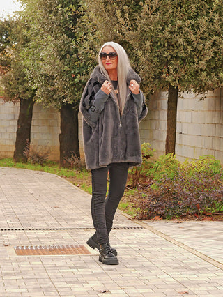 Frau trägt die OFF#DLY FakeFur Jacke Rom asphalt; luxuriöser, kuscheliger Kunstpelz, modern oversize geschnitten, über schwarzem Outfit mit Kapuze und Reißverschluss, ideal für stilvolle Winterlooks.