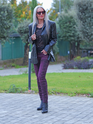 Frau im Park trägt OFF#DLY Denim Eva bordeaux, schmal geschnittene Hose mit moderner Waschung. Kombiniert mit einem schwarzen Blazer und Stiefeln, betont sie stilvoll feminine Outfits.