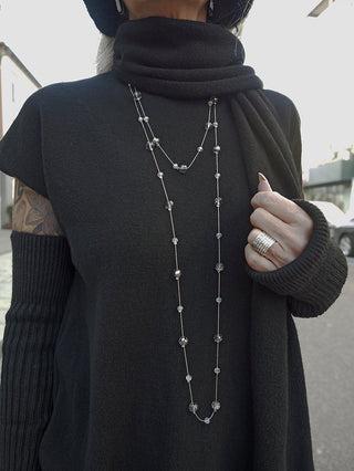 OFF#DLY Kette Riga grey/silver, eine lange, zarte Halskette aus silberfarbenem Metall mit kleinen facettierten Glasperlen, getragen über schwarzem Strick und kombiniert mit einem breiten silbernen Ring und Tattoo sichtbar.