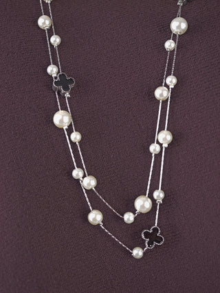 OFF#DLY Kette Cross black/silver: Eine lange silberne Kette mit runden weißen Kunstperlen und kleinen schwarzen Kleeblatt-Anhängern, präsentiert auf einem dunkelvioletten Stoff.