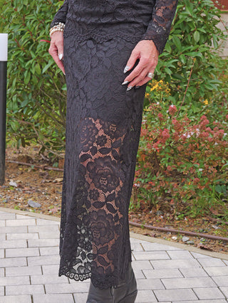 Person trägt den OFF#DLY Rock Resi black, einen eleganten, figurbetonten schwarzen Spitzenrock mit floralen Mustern, kombiniert mit schwarzen Stiefeln, verleiht er einen modernen, femininen Look.