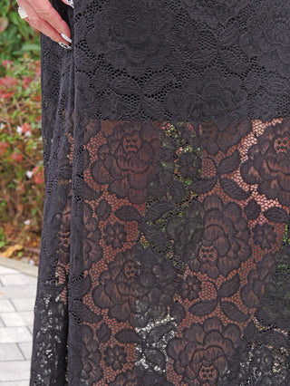 Nahaufnahme des OFF#DLY Rock Resi black, zeigt florale Spitzenmuster mit Rosen und Blättern. Eine Hand mit schwarz-weiß lackierten Nägeln berührt den Rock, der durchscheinend die Beine umspielt.