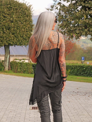 Eine Person von hinten zeigt das OFF#DLY Top Spitze Veronika black mit lockerer Passform und zarter Spitze am Ausschnitt, kombiniert mit dunklen Cargo-Hosen in einer parkähnlichen Umgebung.