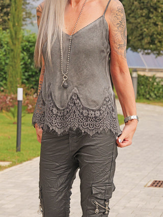 Person trägt das OFF#DLY Top Spitze Allegra asphalt mit zarter Spitzenbordüre und verstellbaren Trägern, kombiniert mit Cargo-Hose und langer Halskette, sichtbar auch Tattoos auf beiden Armen.