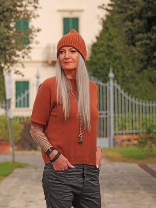 Frau trägt den OFF#DLY Pulli Tina zimt, ein rustfarbenes Kurzarm-Basic mit schmalem Schnitt, kombiniert mit lockeren schwarzen Hosen. Perfekt für einen stilvollen, modernen Look im Herbst.