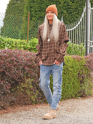 Person trägt die OFF#DLY Bluse Hilde braun mit Karomuster, über schwarzem Top. Die Bluse ist locker geschnitten, Button-Down, Ärmel hochgekrempelt, ideal für einen lässigen Herbstlook.