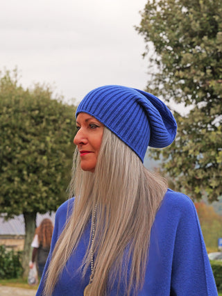 Frau im Profil trägt die OFF#DLY Mütze Anna royalblue, eine gerippte Strickmütze, passend zu ihrem blauen Oberteil. Ihr langes, silberblondes Haar und roter Lippenstift betonen den Look.