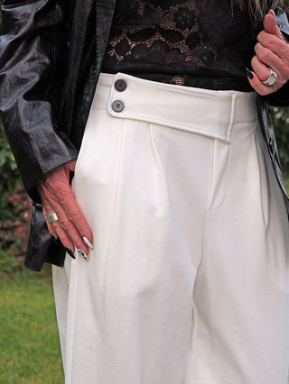 Nahaufnahme der OFF#DLY Hose Moniga white: Hochgeschnitten, weit geschnitten, weiße Hose mit doppeltem Knopfverschluss, kombiniert mit schwarzer Spitze und Lederjacke. Perfekt für einen stilvollen, modernen Look.