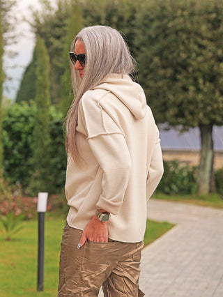 Person von hinten auf einem Weg, trägt den OFF#DLY Hoody (Strick) Daria beige mit Kapuze, lässiger Passform und Ton-in-Ton Logo-Stickerei, kombiniert mit glänzender Hose.