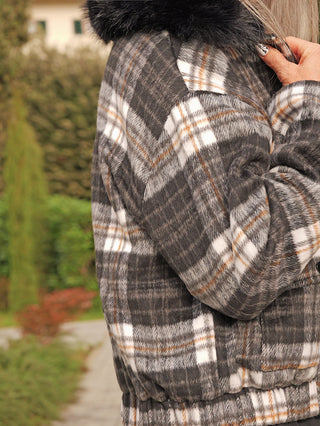 Nahaufnahme einer Person, die draußen eine OFF#DLY Jacke Checker black/grey trägt, mit grauem Karomuster und schwarzem Kunstfellkragen, während sie ihr Haar oder den Kragen anpasst.