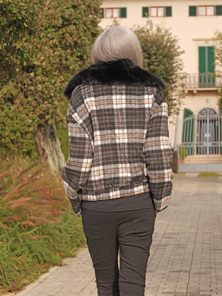 Person trägt die OFF#DLY Jacke Checker black/grey mit schwarzem Kunstfellkragen, während sie einen gepflasterten Weg entlanggeht, der zu einem Haus führt.