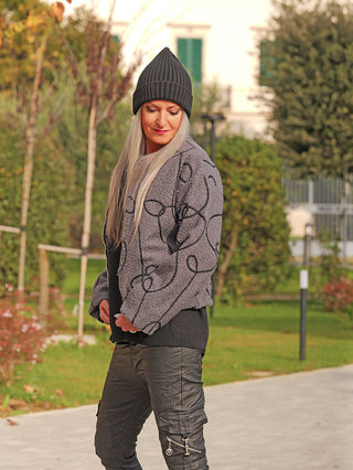 Frau im Park trägt OFF#DLY Jacke Alina asphalt, mit schwarzem Muster und Reißverschluss, ideal für Herbst/Winter. Kombiniert mit schwarzer Hose, die Jacke bietet warmen Teddy-Stoff und ist vielseitig tragbar.