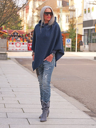 Person trägt den OFF#DLY Poncho Teddy blue, einen locker fallenden, kapuzenbewehrten Teddy-Poncho, über einem Langarmshirt und Jeans in urbaner Szenerie. Ideal für kühle Tage.