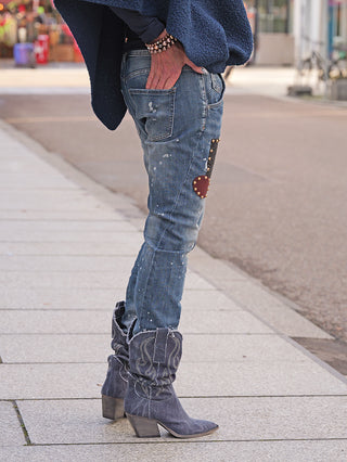 OFF#DLY Destroy Denim Dora midblue Jeans, schmal geschnitten mit leichten Paint-Splatter-Details und einem Nietendekor-Patch. Kombiniert mit dunkelblauen Cowboy-Stiefeln und Armbändern, präsentiert sie einen urbanen Look.