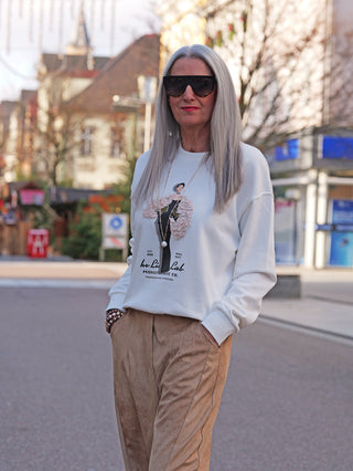 Frau trägt OFF#DLY Sweat Laura white, ein off-white Sweatshirt mit 3D-Print, kombiniert mit hellbraunen Hosen. Stylisch und bequem, ideal für modische Herbst- und Winterlooks.