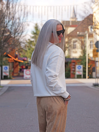 Person trägt das OFF#DLY Sweat Laura white mit auffälligem Print und dreidimensionalen Texturdetails, kombiniert mit hellbraunen Wildlederhosen. Gemütlicher, figurumspielender Schnitt, ideal für stilvolle, komfortable Outfits.