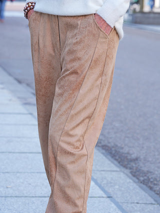 Person in OFF#DLY Hose Velourstoff Salo camel, elegant im Veloursleder-Look mit seitlichen Taschen, leicht lockerer Passform. Sichtbarer Bund eines weichen weißen Pullovers und Armband am Handgelenk.