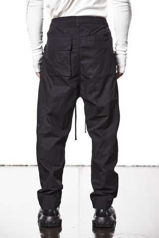 Thom Krom Hose MP25 black Cargo Trousers mit elastischem Bund und Kordelzug, metallisierter Baumwolle für schimmernden Look. Sichtbar: lockere Passform, tiefer Schritt, Patch-Taschen; kombiniert mit klobigen schwarzen Stiefeln.